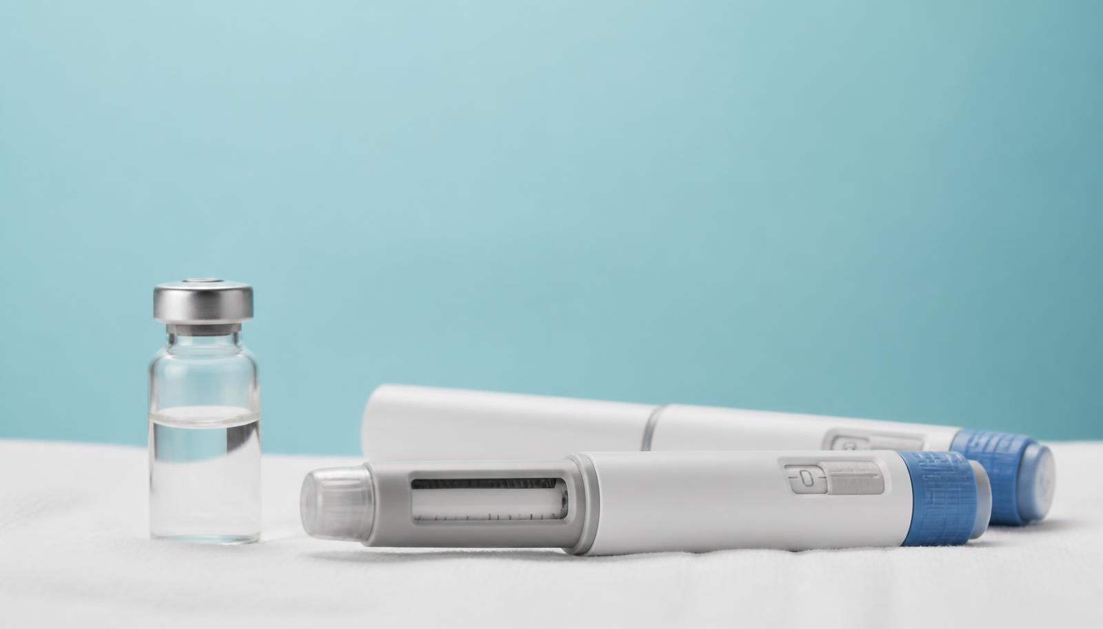 Two unbranded weekly injection pens and a glass vial on a clinical white surface